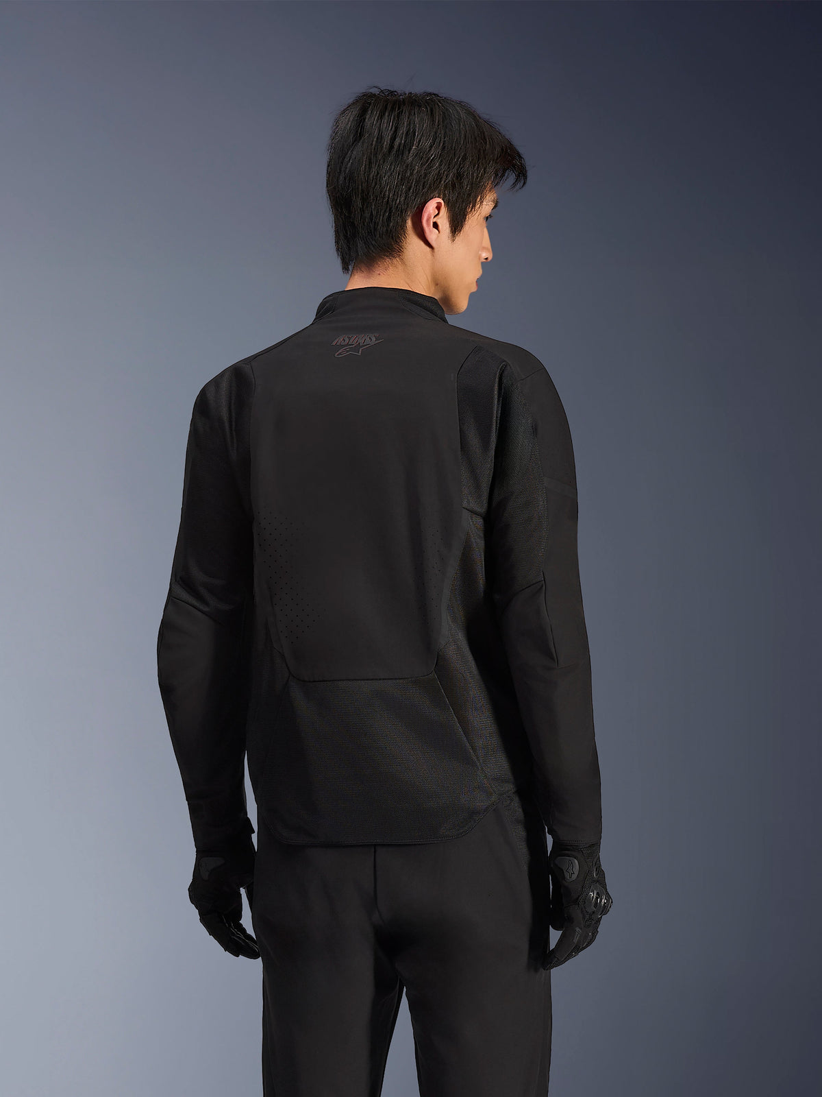 Alpinestars Aeroshell Airflow Jas, Black Anthracite, achteraanzicht van sportieve motorjas met lasergeperforeerde ventilatiezones en 2D-meshpanelen, verlengde achterkant voor extra bedekking, gedragen met zwarte motorhandschoenen