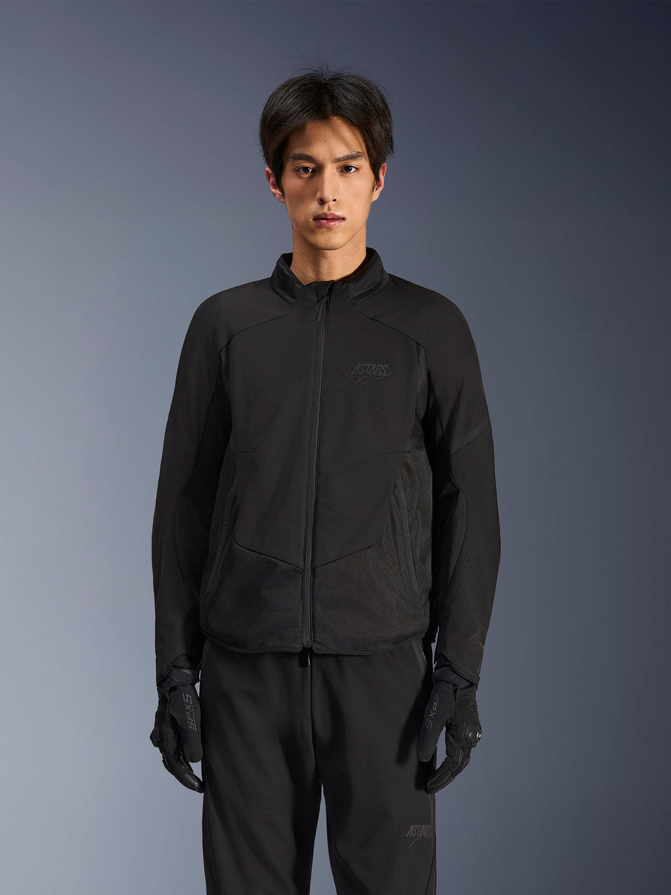 Alpinestars Aeroshell Airflow jas in Black Anthracite, lichtgewicht motorjas met laser-geperforeerde ventilatie op de borst en mouwen, ademende mesh-panelen en een gestroomlijnd sportief ontwerp, gedragen door een model met zwarte motorhandschoenen.