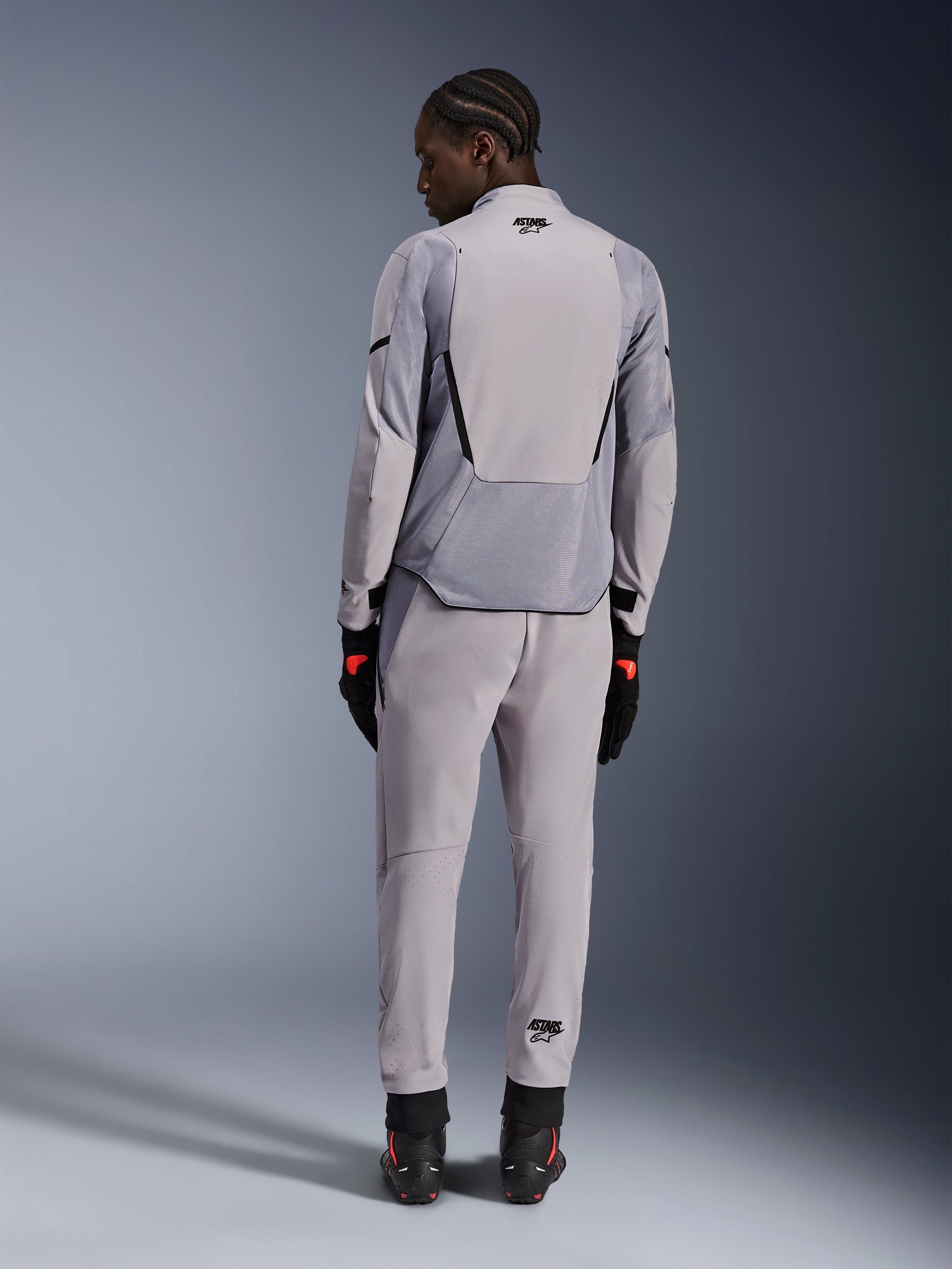 Alpinestars Aeroshell Airflow Jas, Mid Gray Anthracite, rugaanzicht op een model, voorzien van technische mesh-panelen en lasergeperforeerde ventilatiezones, gedragen met bijpassende grijze broek en zwarte motoruitrusting, sportieve pasvorm voor hoge prestaties