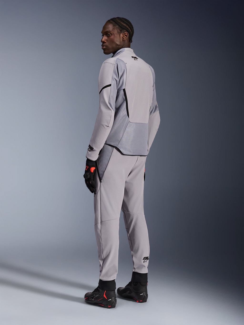 Alpinestars Aeroshell Airflow Jacket in Mid Gray Anthracite, worn with matching pants and black racing gloves, back view showing laser-perforated panels and athletic sport fit, professional motorcycle apparel