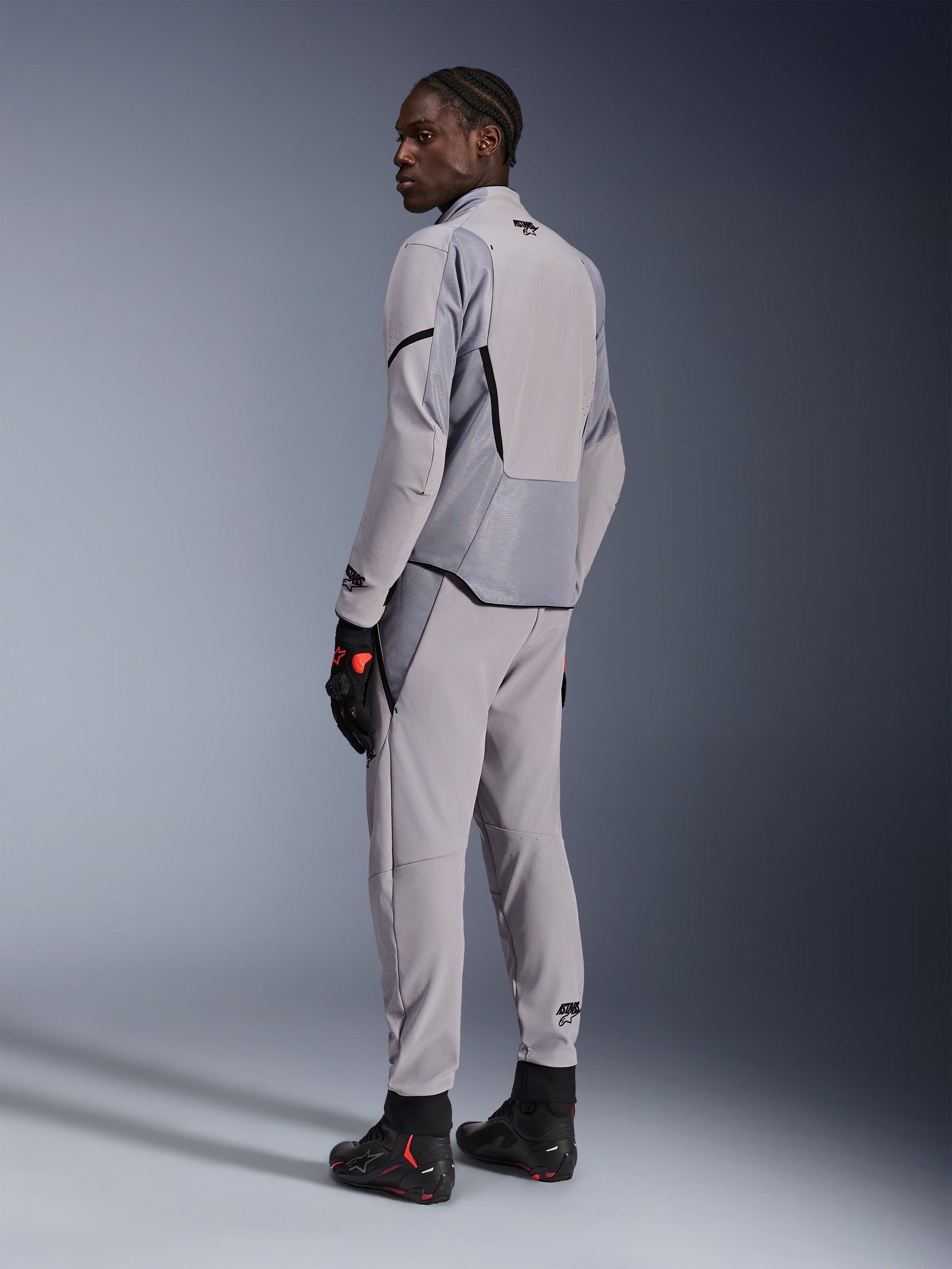Alpinestars Aeroshell Airflow Jas in Mid Gray Anthracite, gedragen met bijpassende broek en zwarte racehandschoenen, achteraanzicht met lasergeperforeerde panelen en atletische sportpasvorm, professionele motorkleding