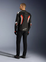 Alpinestars T-GP Air Jacket, Black Red Fluo motorcycle jacket, rear view on a model, featuring mesh ventilation panels, aerodynamic hump, and white external protectors on elbows and shoulders, worn with black pants and riding shoes