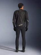 Alpinestars T-GP Air Jacket, zwart, achteraanzicht van een man die de textiele motorjas draagt, voorzien van mesh ventilatiepanelen, een aerodynamische bult en witte Alpinestars-logo's op de onderrug en ellebogen, gedragen met een zwarte motorbroek en handschoenen