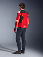 Alpinestars T-GP Air Jacket, achteraanzicht van een man die een felrode en fluo rode textieljas draagt met zwarte mesh-panelen en witte sliders, gecombineerd met een donkerblauwe jeans en zwarte motorschoenen, sportieve motoruitrusting