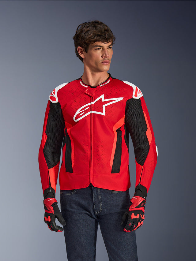 Alpinestars T-GP Air Jacket, motorjas, felrood en zwart met wit logo, voorzien van geperforeerde mesh ventilatiepanelen, gedragen met bijpassende handschoenen en donkere spijkerbroek, sportief ontwerp voor rijden in warm weer