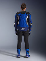 Alpinestars T-GP Air jas, Bright Blue Navy White, achteraanzicht met aerodynamische hump en mesh ventilatiepanelen, wit Alpinestars-logo op de onderrug, gedragen met zwarte broek en blauwe racelaarzen