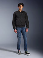 Alpinestars Flight Air Jacket, zwart, stedelijk geïnspireerde motorjas in bomberstijl met 3D mesh-panelen en wit logo op de borst, gedragen door een model met blauwe jeans en zwarte sneakers, eigentijdse motorkleding