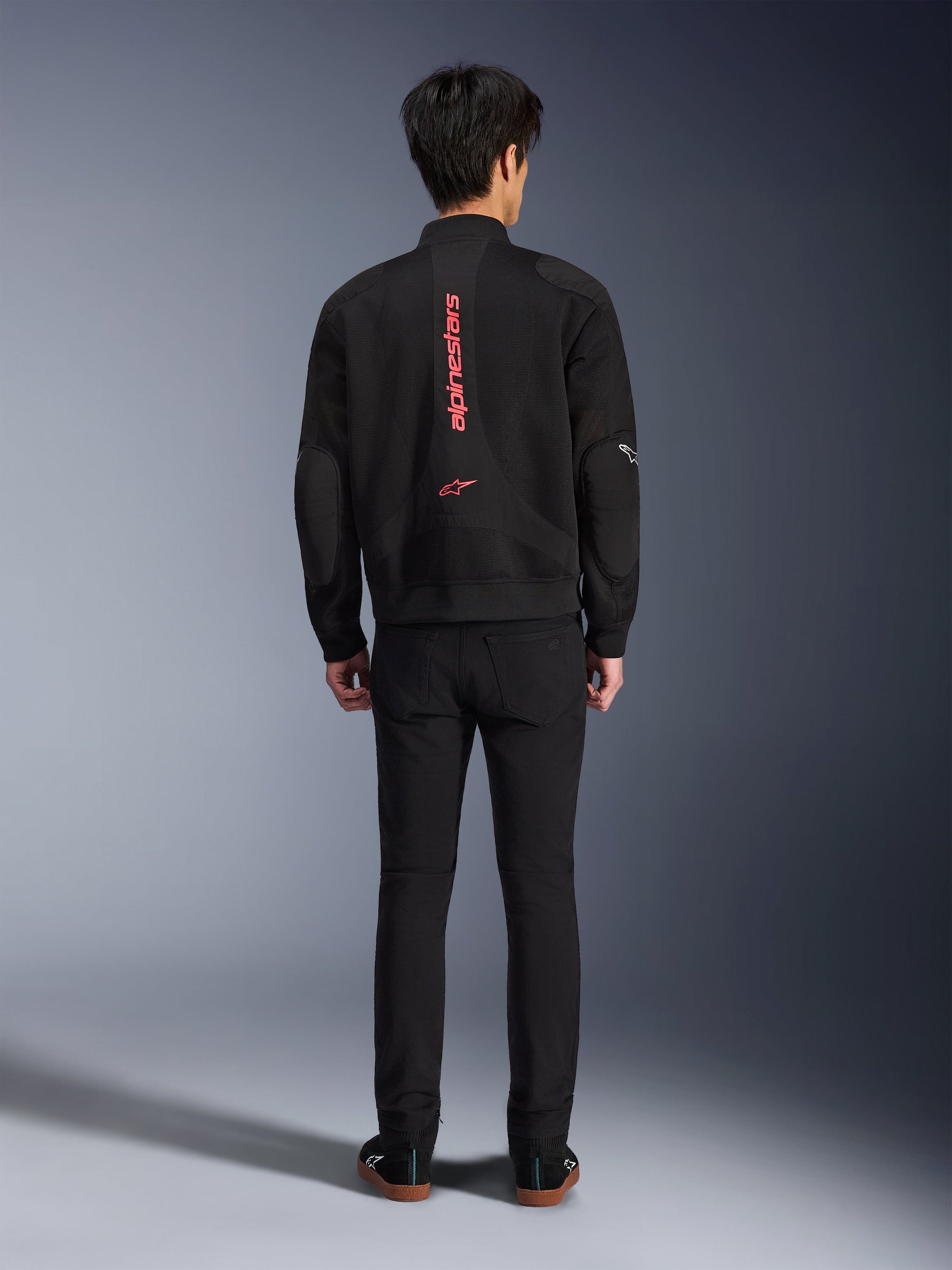 Alpinestars Flight Air Jacket in Black Bright Red, achteraanzicht van een stedelijke motorjas in bomberstijl, voorzien van verticale rode Alpinestars-branding en logo op de rug, lichtgewicht 3D mesh-constructie, gedragen met een zwarte broek voor een eigentijdse look.