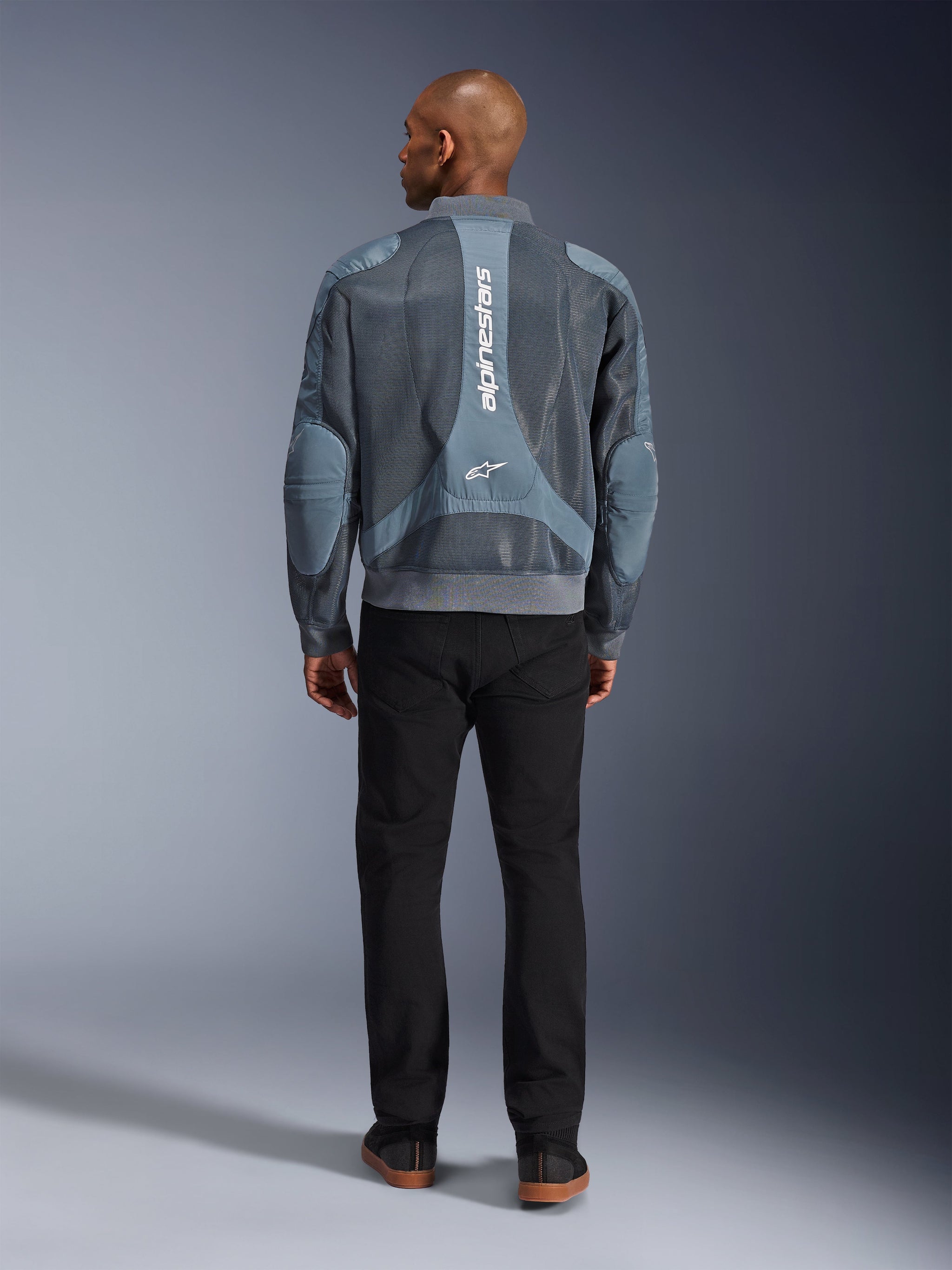 Alpinestars Flight Air Jacket in Storm Gray, back view of male model wearing urban-style motorcycle jacket with 3D mesh panels and vertical Alpinestars branding, paired with black pants for a modern commuter look