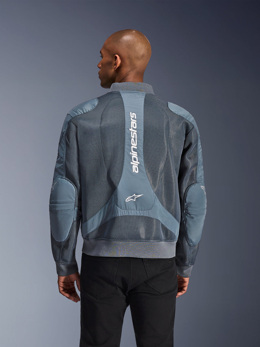 Alpinestars Flight Air Jacket in Storm Gray, achteraanzicht op een model, stedelijke motorjas voorzien van uitgebreide 3D-meshpanelen, verticale Alpinestars-branding op de rug en een geribbelde zoom en kraag in bomberstijl.