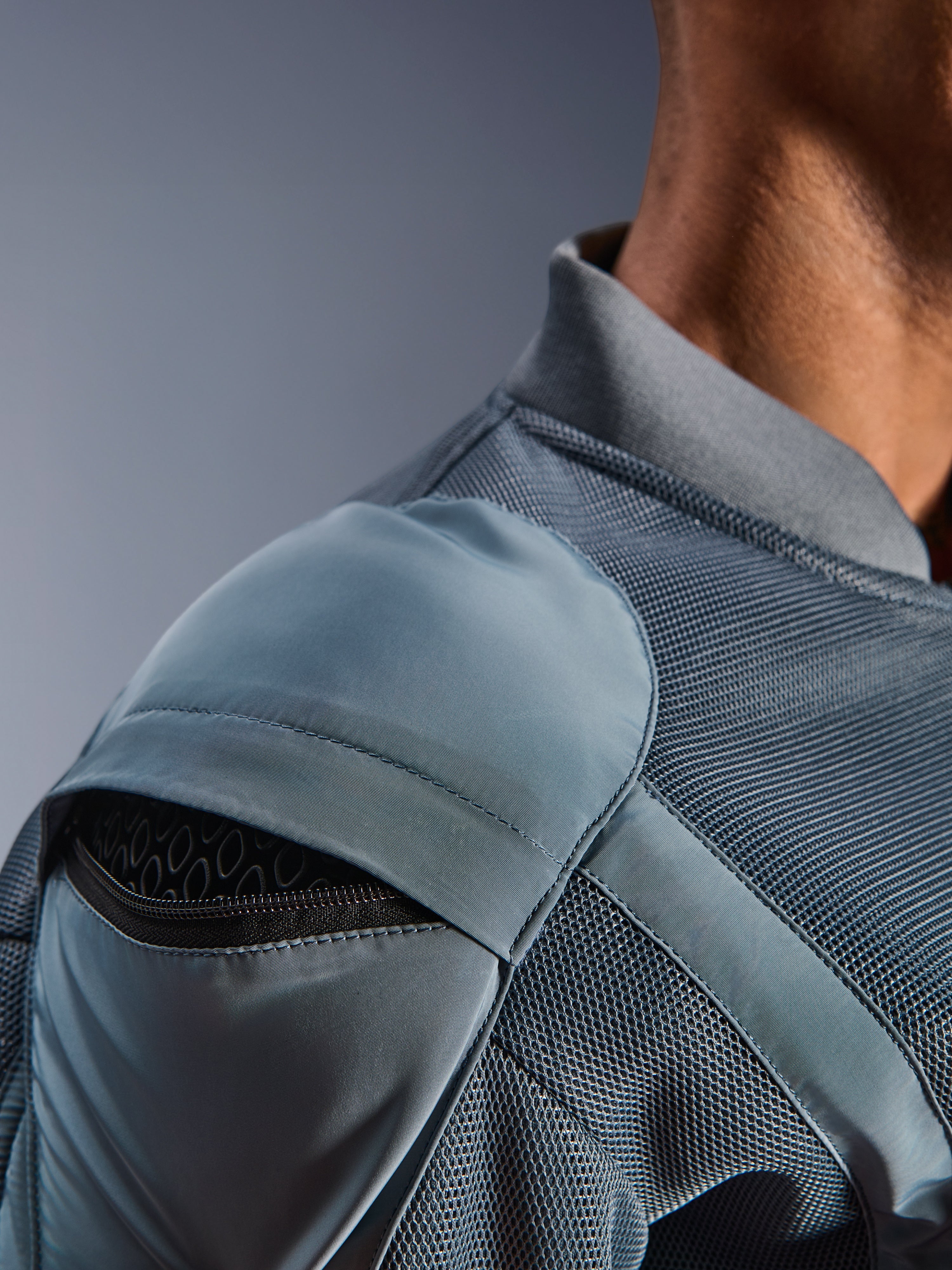 Close-up van het Alpinestars Flight Air Jacket in Storm Gray, met de nadruk op de externe schouderprotectiezak met zichtbaar honingraat-pantser, 3D mesh ventilatiepanelen en geribbelde kraag voor technisch stedelijk motorrijden