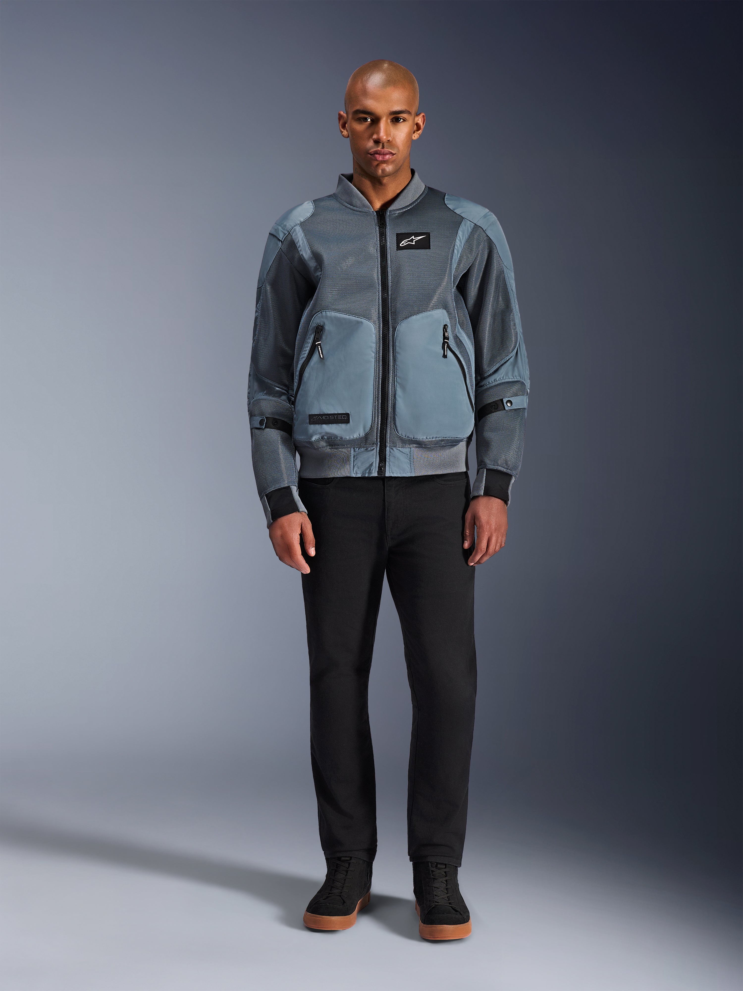 Alpinestars Flight Air jas in Storm Gray, urban bomber-geïnspireerde motorjas met 3D meshpanelen en stevige voorzakken, gedragen door een man met een zwarte broek en zwarte hoge sneakers, moderne street-style motorkleding