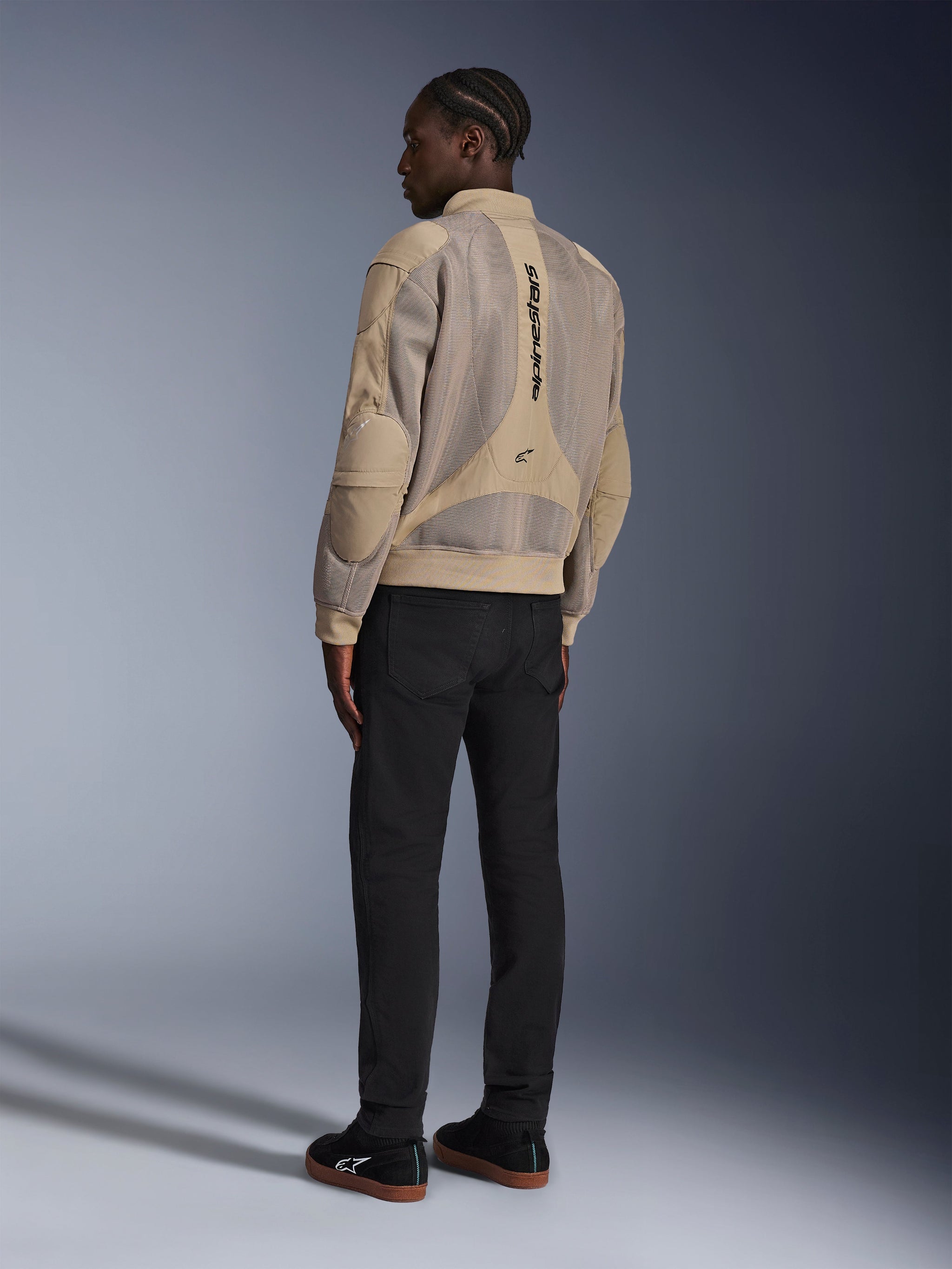 Alpinestars Flight Air Jacket, urban textile motorcycle jacket, Brown, back view showing large 3D mesh panels and vertical logo, bomber-style silhouette with ribbed collar and hem, paired with black pants and black shoes for street-inspired riding style.