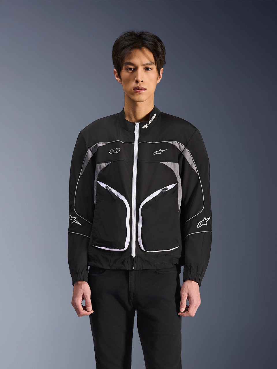 Alpinestars Unite Jacket, minimalist urban motorcycle jacket, Black and Dark Gray with white accents, features a white front zipper, reflective piping, and Alpinestars branding on the chest and sleeves, contemporary streetwear style for riders.