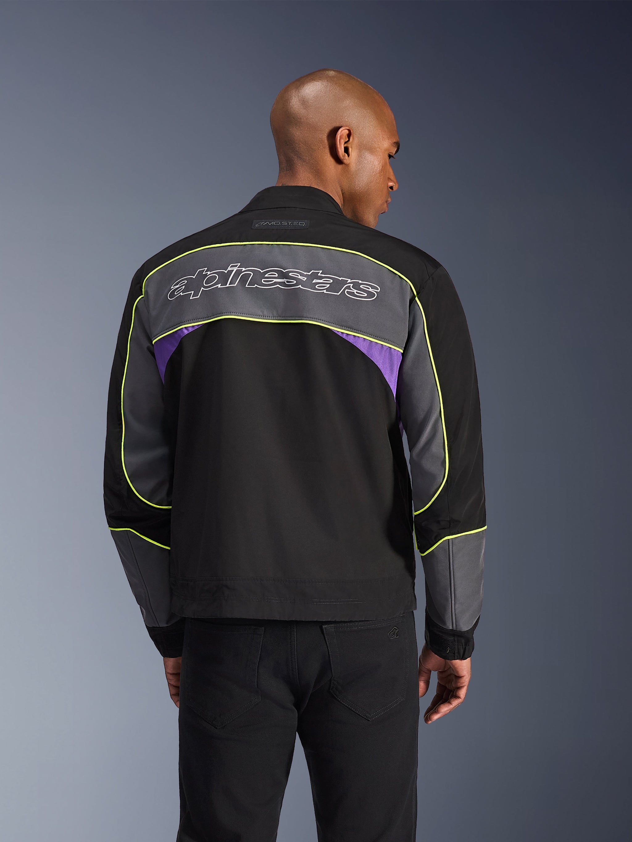 Alpinestars Unite Jacket, Urban motorjas, Black Asphalt Violet, achteraanzicht met grijze panelen en violetkleurige accenten, limegele biesjes, groot Alpinestars-woordmerk op de bovenrug, minimalistisch streetwear-ontwerp