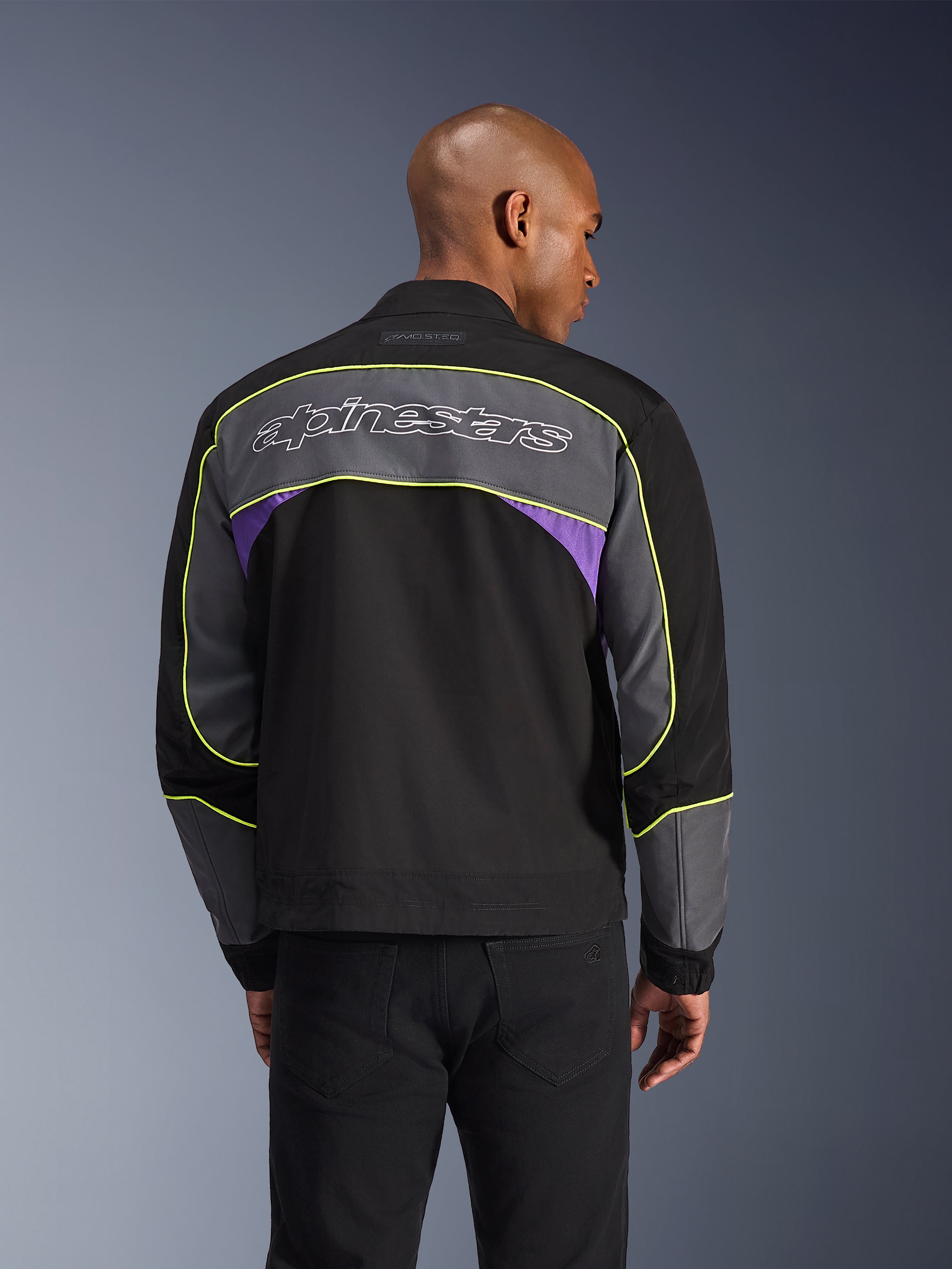 Alpinestars Unite Jacket, Urban motorjas, Black Asphalt Violet, achteraanzicht met grijze panelen en violetkleurige accenten, limegele biesjes, groot Alpinestars-woordmerk op de bovenrug, minimalistisch streetwear-ontwerp