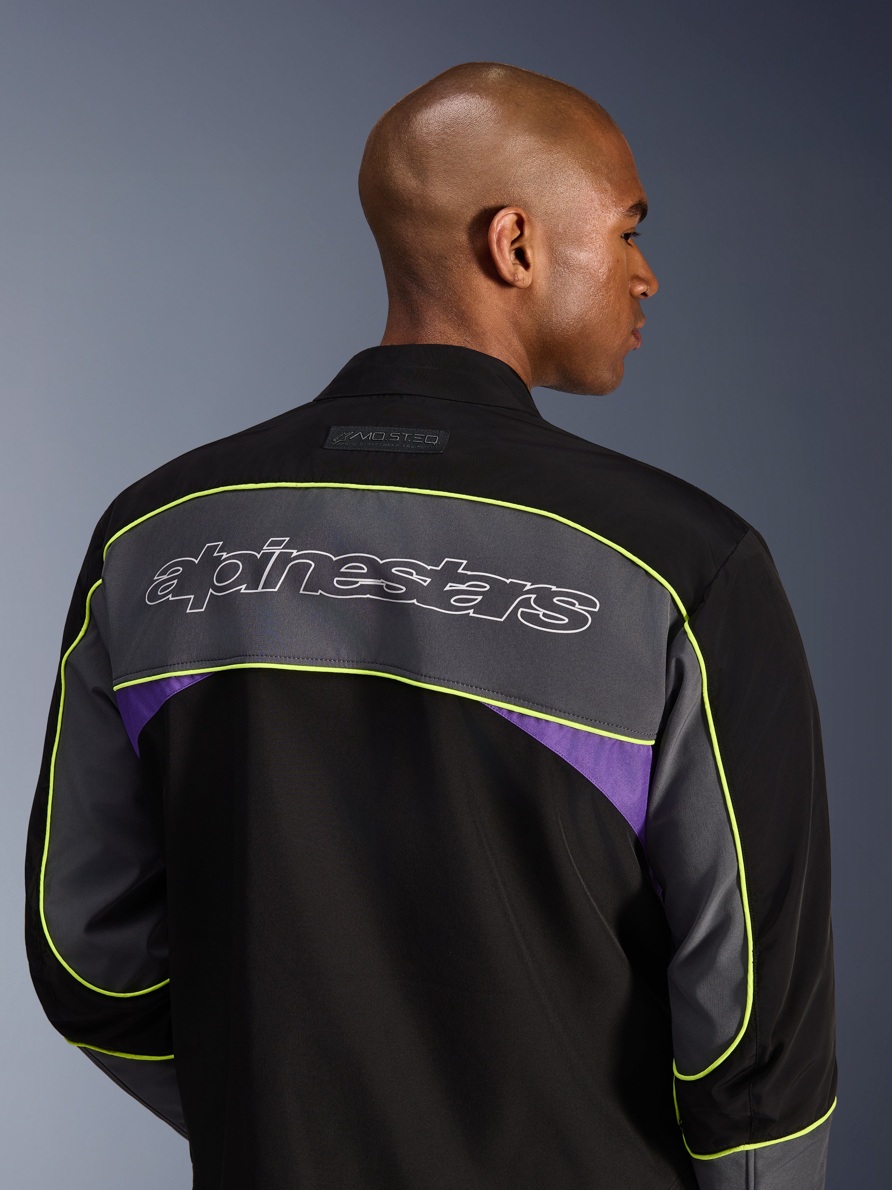 Alpinestars Unite Jacket, stedelijke motorjas, Black Asphalt Violet, achteraanzicht met een groot grijs schouderpaneel met Alpinestars-logo, neongele bies en violette accenten op een 3-laagse softshell-constructie