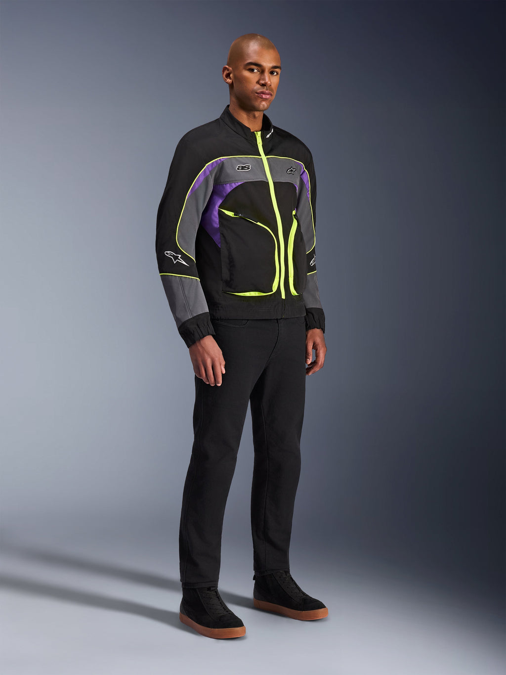 Alpinestars Unite Jacket, stedelijke motorjas, Black Asphalt Violet met neongele accenten, gedragen door model met zwarte broek en sneakers, eigentijdse streetwear-stijl voor stedelijke ritten