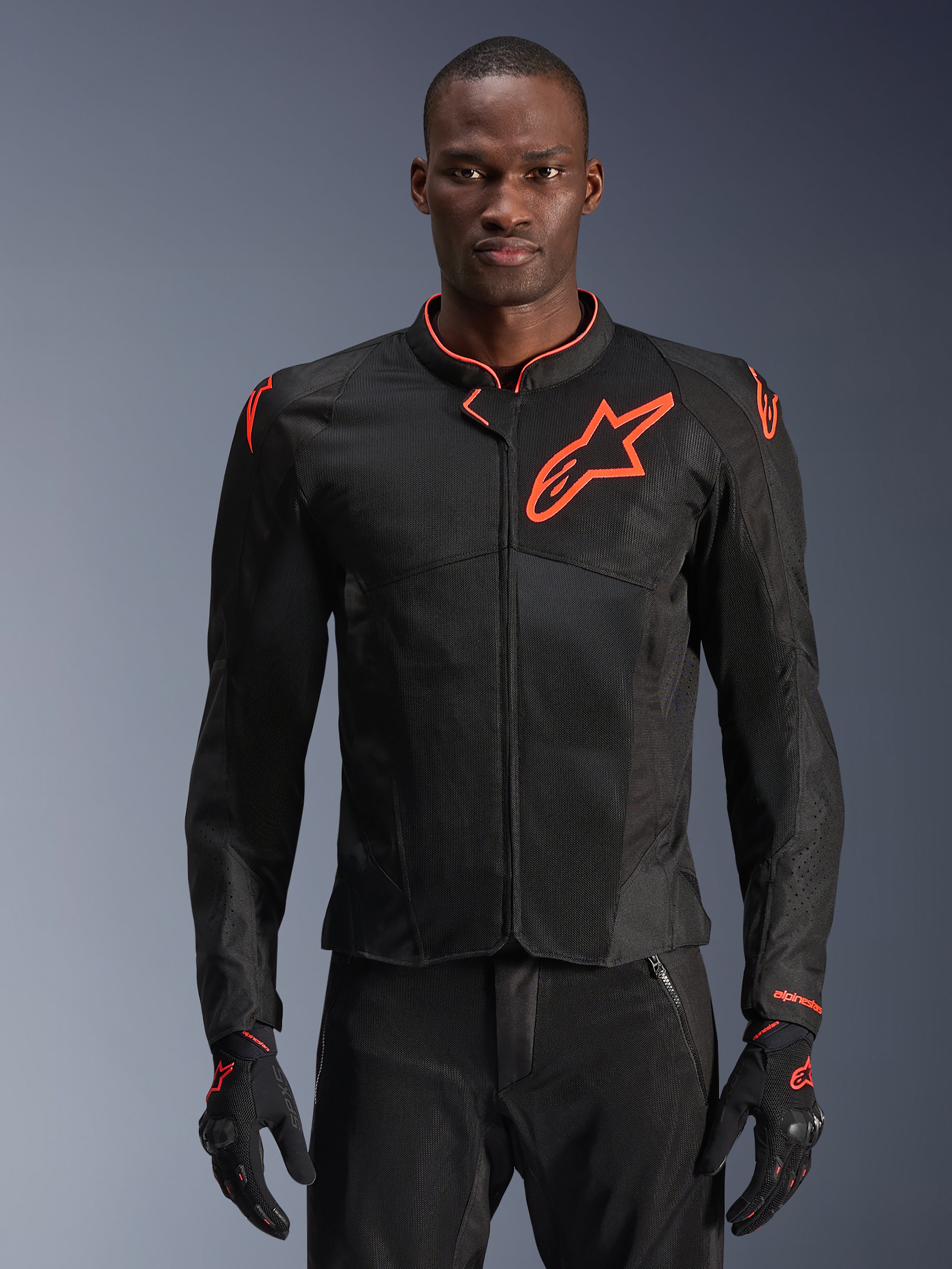 Alpinestars Viper Air V4 motorjas, zwart en fluorood motorjack, geventileerde mesh-constructie met opvallend rood sterlogo, gedragen door model met bijpassende handschoenen, sportief performance-design
