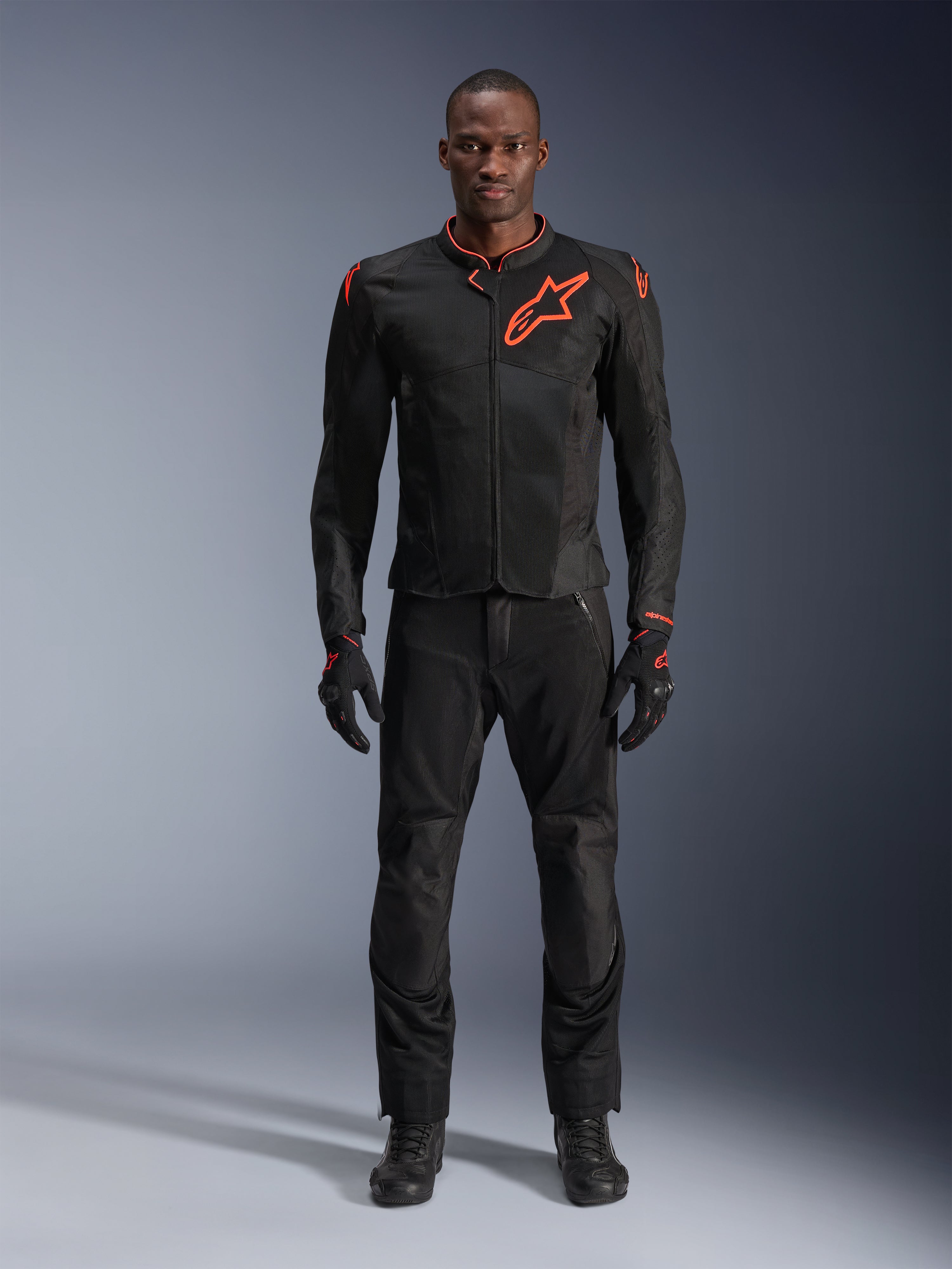 Alpinestars Viper Air V4 Jas in Black Red Fluo, motorjas gedragen door een model met bijpassende zwarte broek en handschoenen, voorzien van mesh-panelen voor luchtstroom en een opvallend rood Alpinestars-logo op de borst, sportieve motoruitrusting