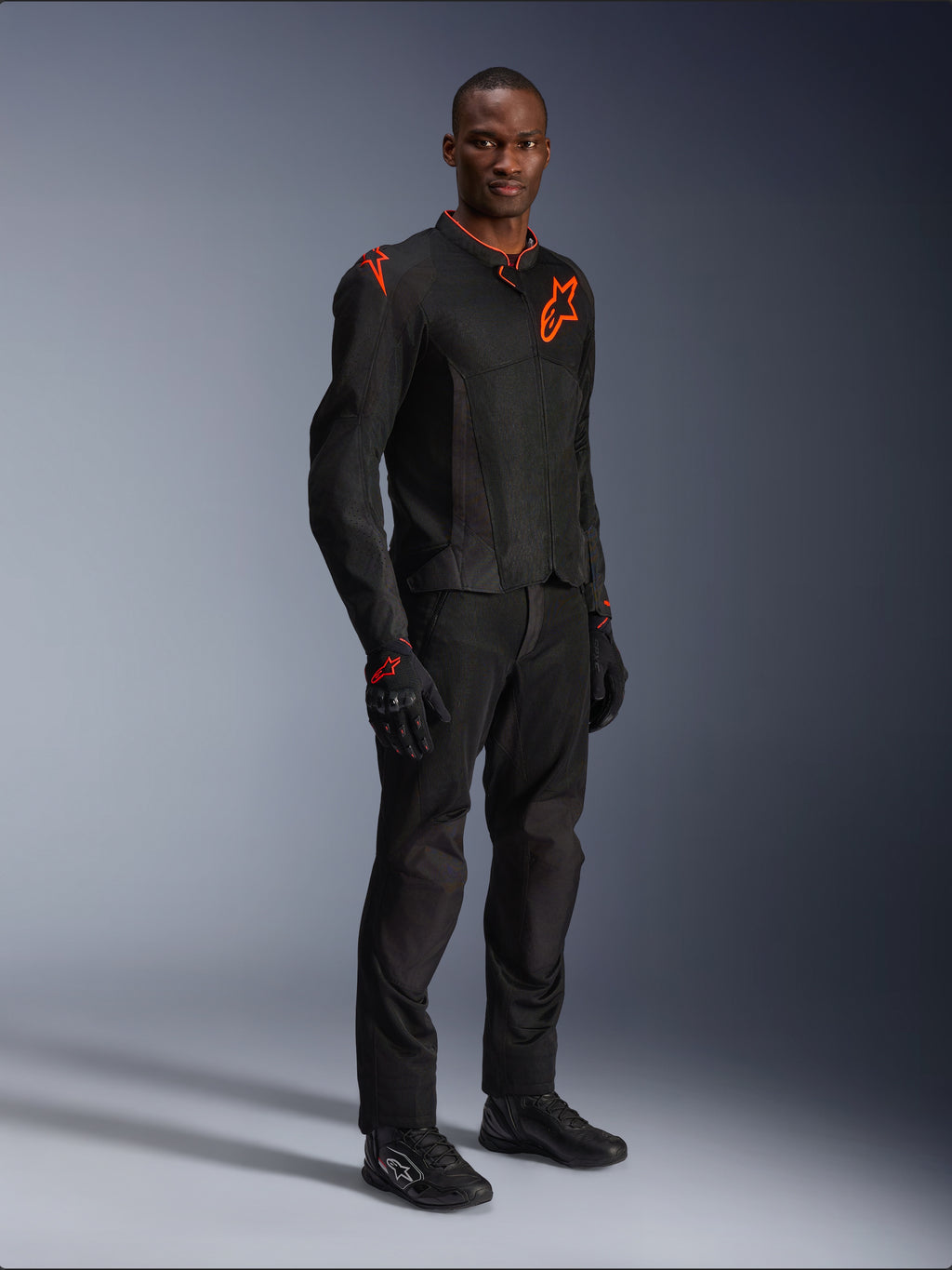 Model draagt Alpinestars Viper Air V4-jas in Black Red Fluo, voorzien van mesh panelen en rode sterlogo's op de borst en schouder, gecombineerd met bijpassende zwarte motorbroek, handschoenen en motorschoenen, professionele motorrijuitrusting voor op de weg