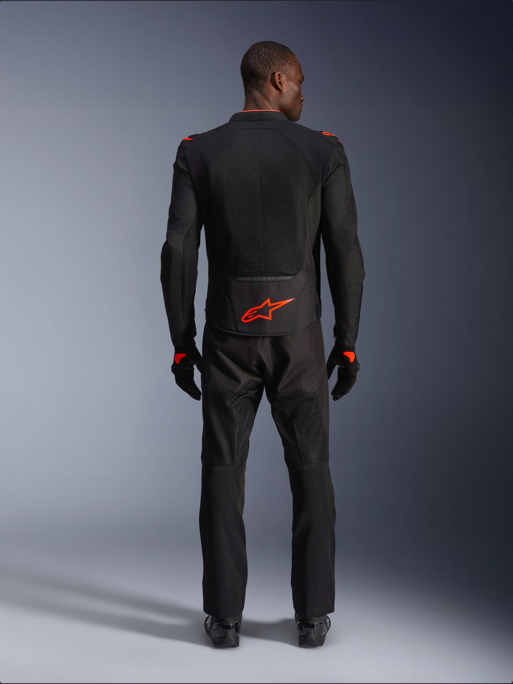 Alpinestars Viper Air V4 Jacket, zwart en fluorood, achteraanzicht op model, gedragen met bijpassende zwarte motorbroek en handschoenen, voorzien van een fel fluorood logo op de onderrug, mesh-constructie voor luchtstroom, atletische pasvorm voor motorrijden op de weg