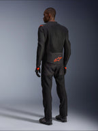 Mannelijke motorrijder van achteren gezien in de Alpinestars Viper Air V4 Jas, Black Red Fluo, met een oranje Astars-logo op de onderrug en schouders, mesh-textielconstructie, gecombineerd met bijpassende zwarte motorbroek en laarzen.