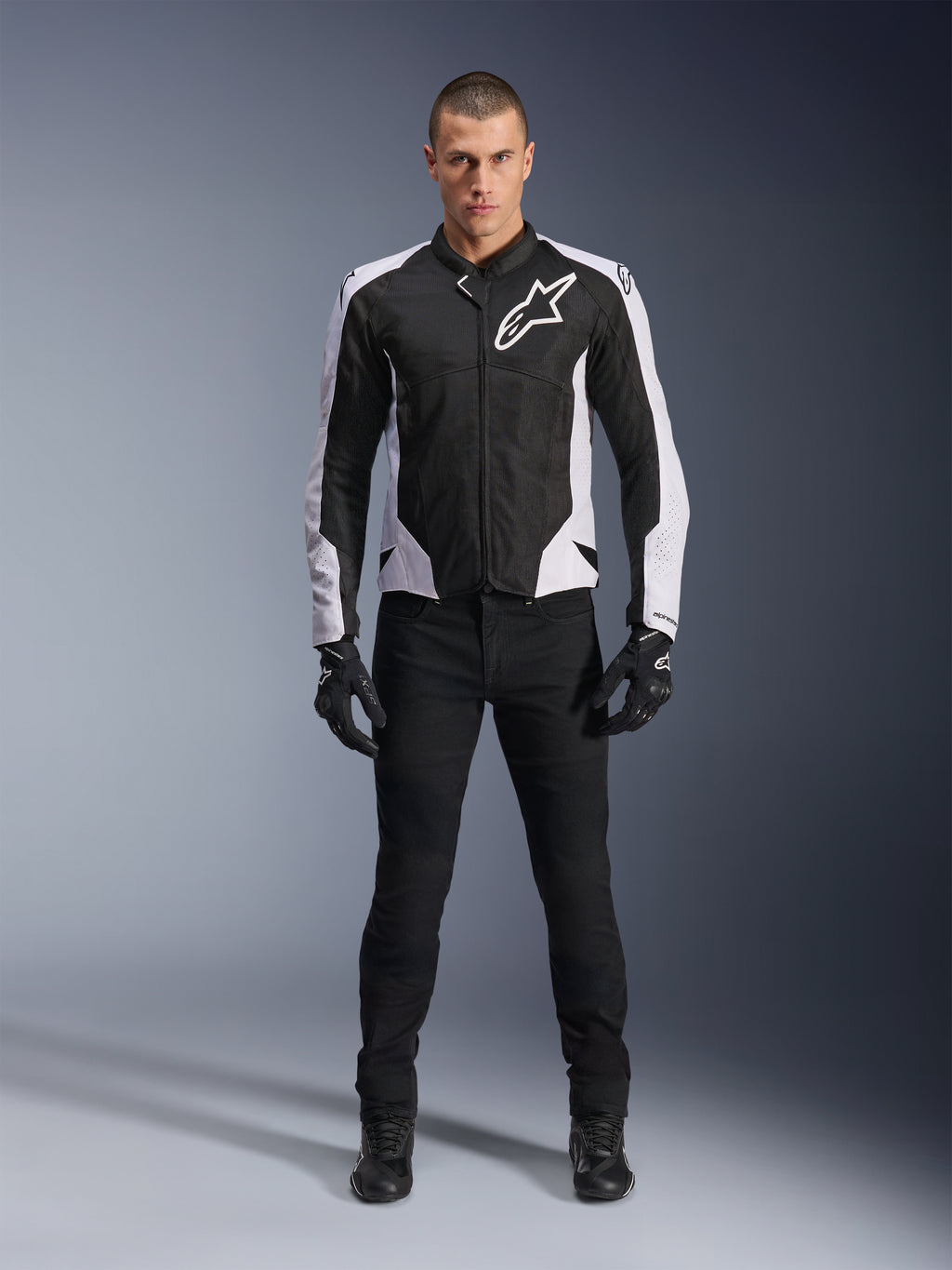 Alpinestars Viper Air V4 Jas, zwart-witte motorjas met groot wit logo op de borst, gedragen door een mannelijk model met zwarte broek en handschoenen, voorzien van meshpanelen voor ventilatie, sportieve motorkleding voor op de weg
