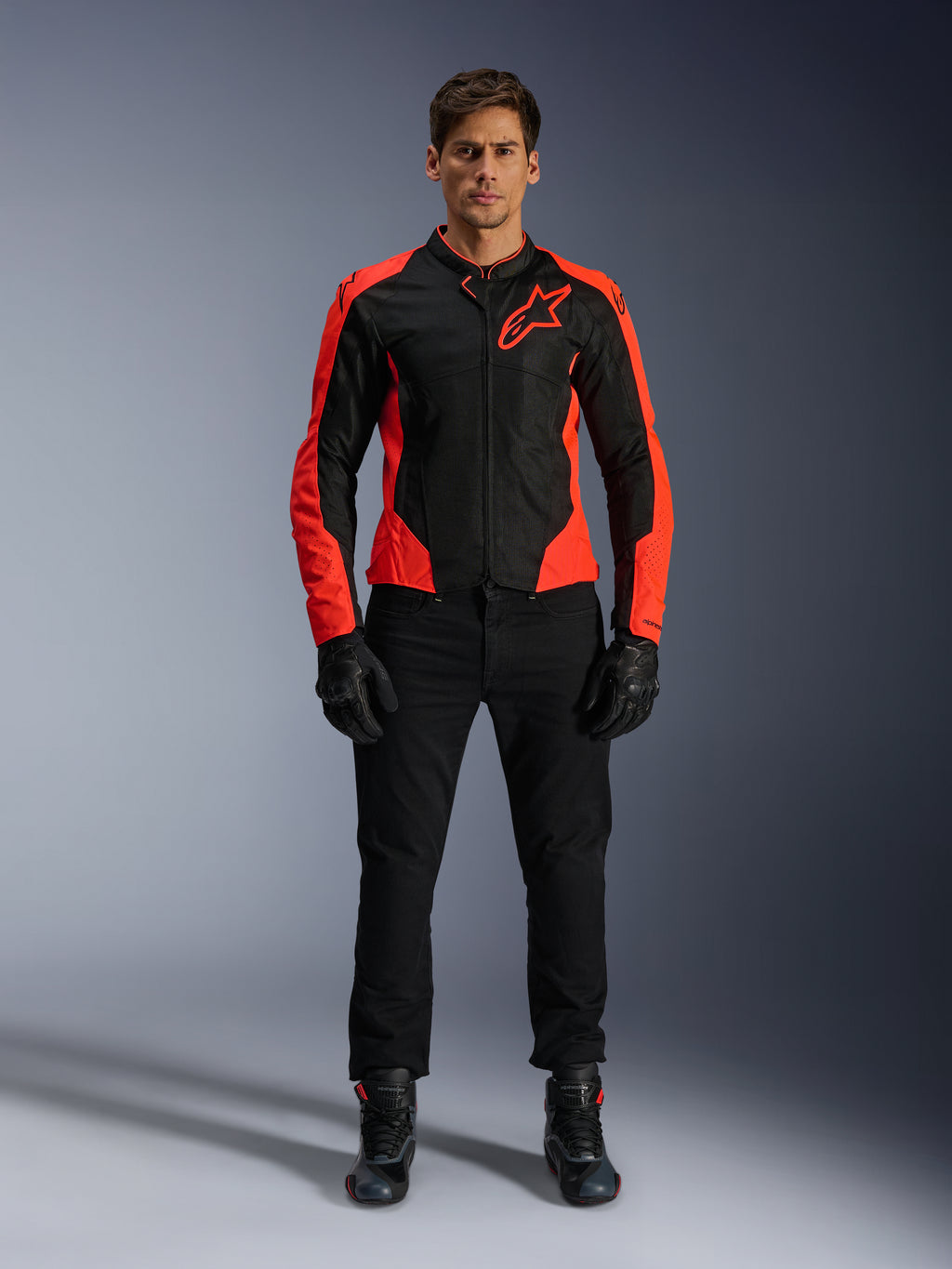 Mannelijk model draagt de Alpinestars Viper Air V4-jas in Red Fluo en Black, gecombineerd met een zwarte motorbroek, handschoenen en laarzen, voorzien van ademende mesh-panelen voor ventilatie en een opvallend sterlogo op de borst, sportieve motorkleding voor op de weg