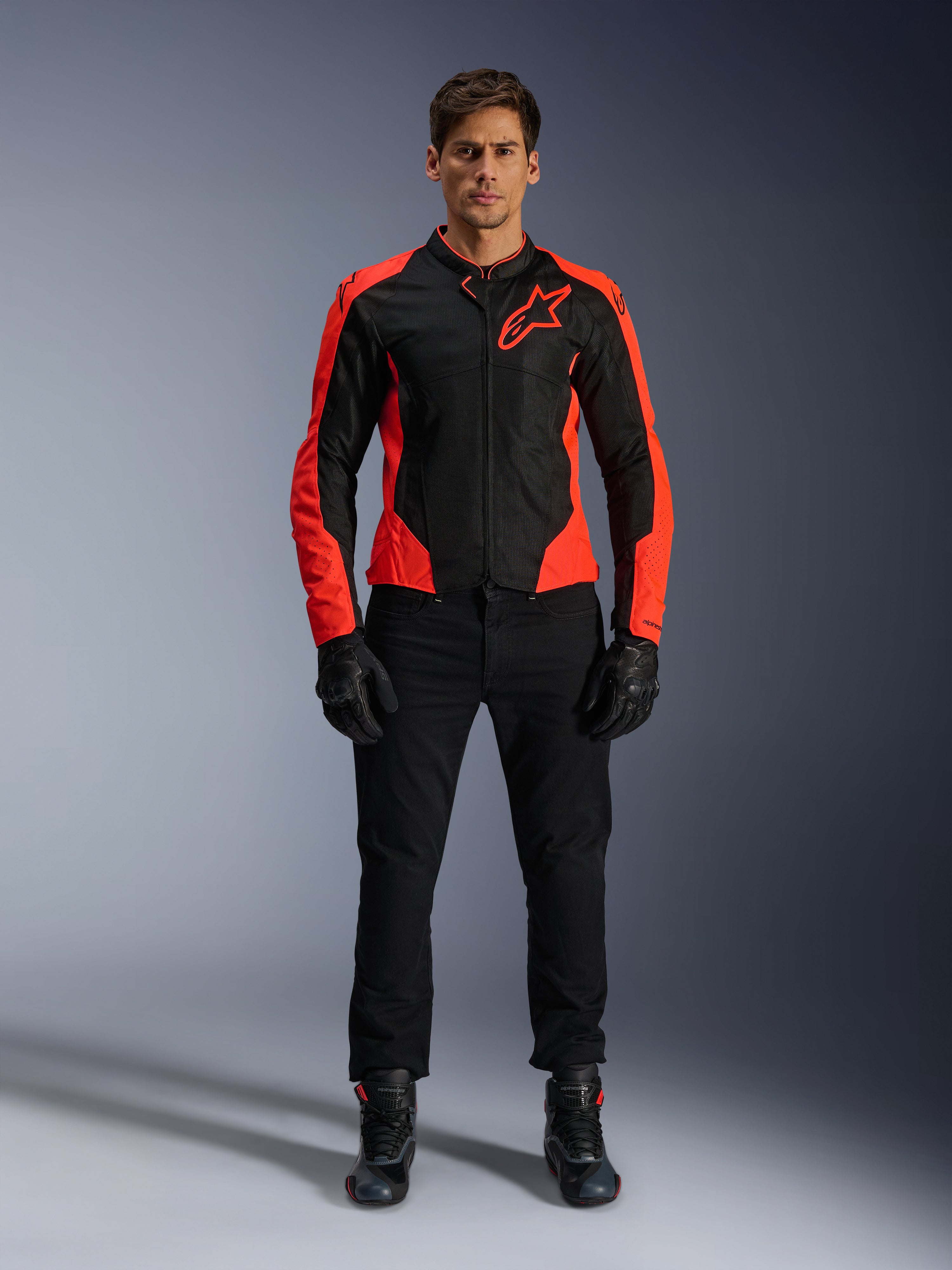 Mannelijk model draagt de Alpinestars Viper Air V4-jas in Red Fluo en Black, gecombineerd met een zwarte motorbroek, handschoenen en laarzen, voorzien van ademende mesh-panelen voor ventilatie en een opvallend sterlogo op de borst, sportieve motorkleding voor op de weg