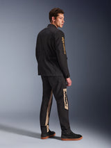 Alpinestars Dice Jacket, stedelijke motorjas, zwart, 3/4 achteraanzicht op model, vintage veldjas-esthetiek met gouden Alpinestars-logo op de mouw, gedragen met bijpassende zwart-beige motorbroek en zwarte sneakers
