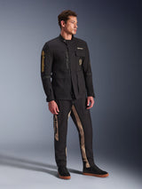 Mannelijk model in Alpinestars Dice Jacket in het zwart, urban motorjas met vintage veldjas-esthetiek, voorzien van meerdere functionele zakken en gouden branding op de mouw, gecombineerd met bijpassende zwart-beige broek en zwarte sneakers