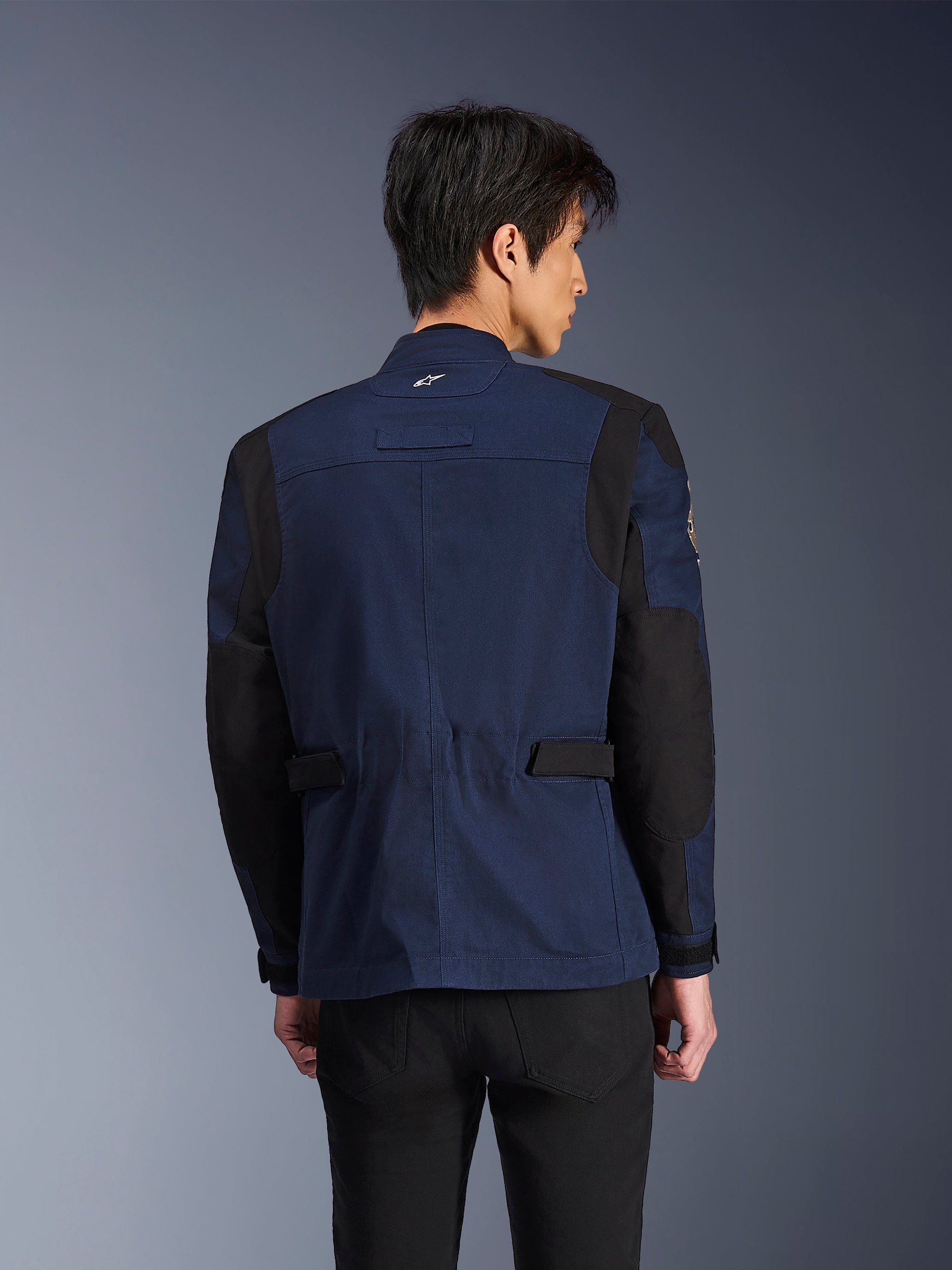 Alpinestars Dice Jacket, donkerblauwe en zwarte urban field motorjas, rugaanzicht gedragen door een man, voorzien van verstevigde zwarte schouder- en elleboogpanelen met verstelbare taillebanden.