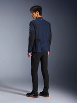 Mannelijk model van achteren gezien, draagt de Alpinestars Dice Jacket in donkerblauw en zwart, gecombineerd met een zwarte broek en zwarte sneakers, urban motorveldjas met geplooide schouders en verstelbare taille-tabs.
