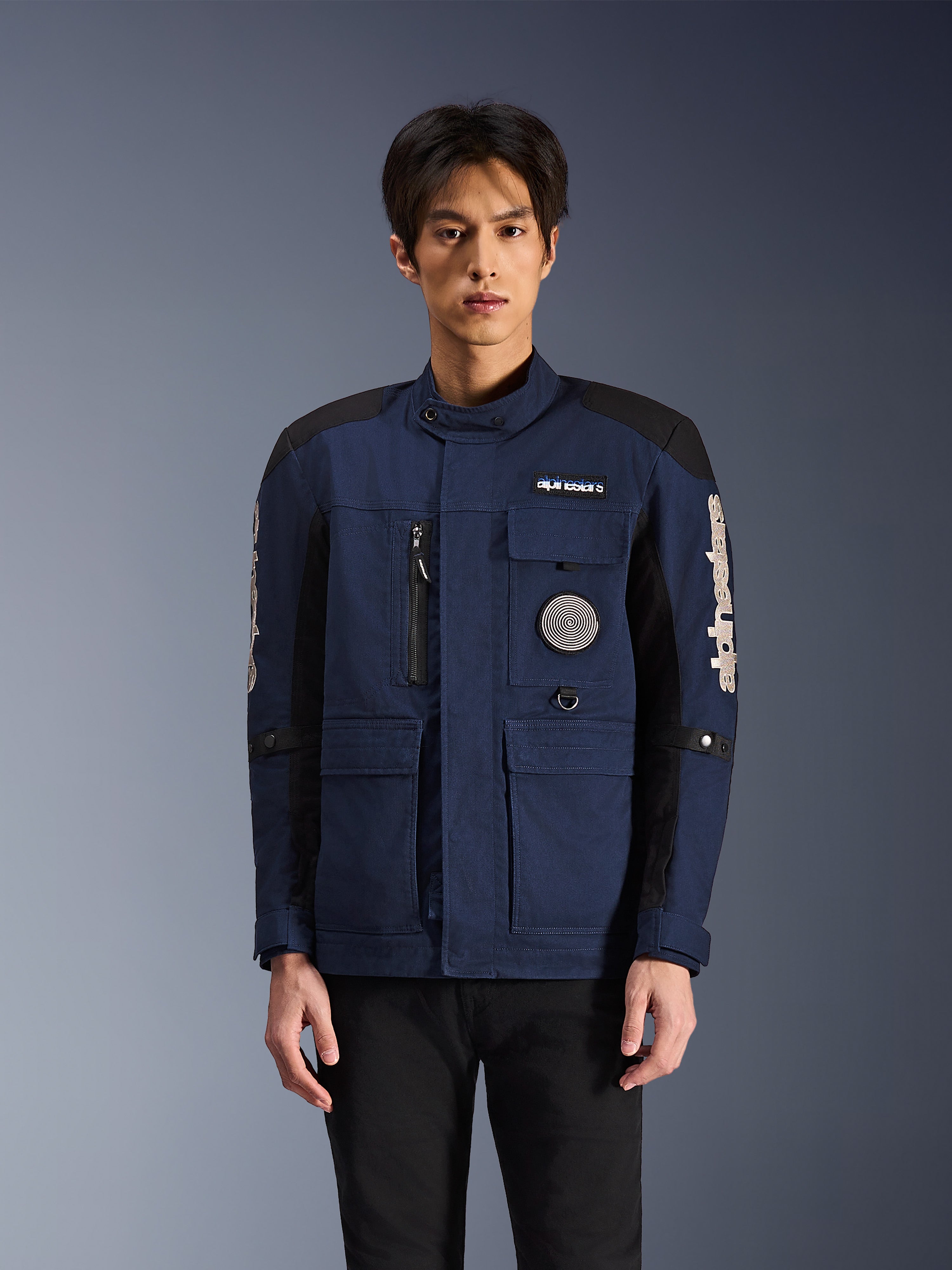 Alpinestars Dice Jacket, stedelijke motorjas, donkerblauw en zwart, veldjas-ontwerp met meerdere zakken, spiraalvormige patch op de borst en witte Alpinestars-branding op de mouwen, moderne op werkkleding geïnspireerde motorkleding