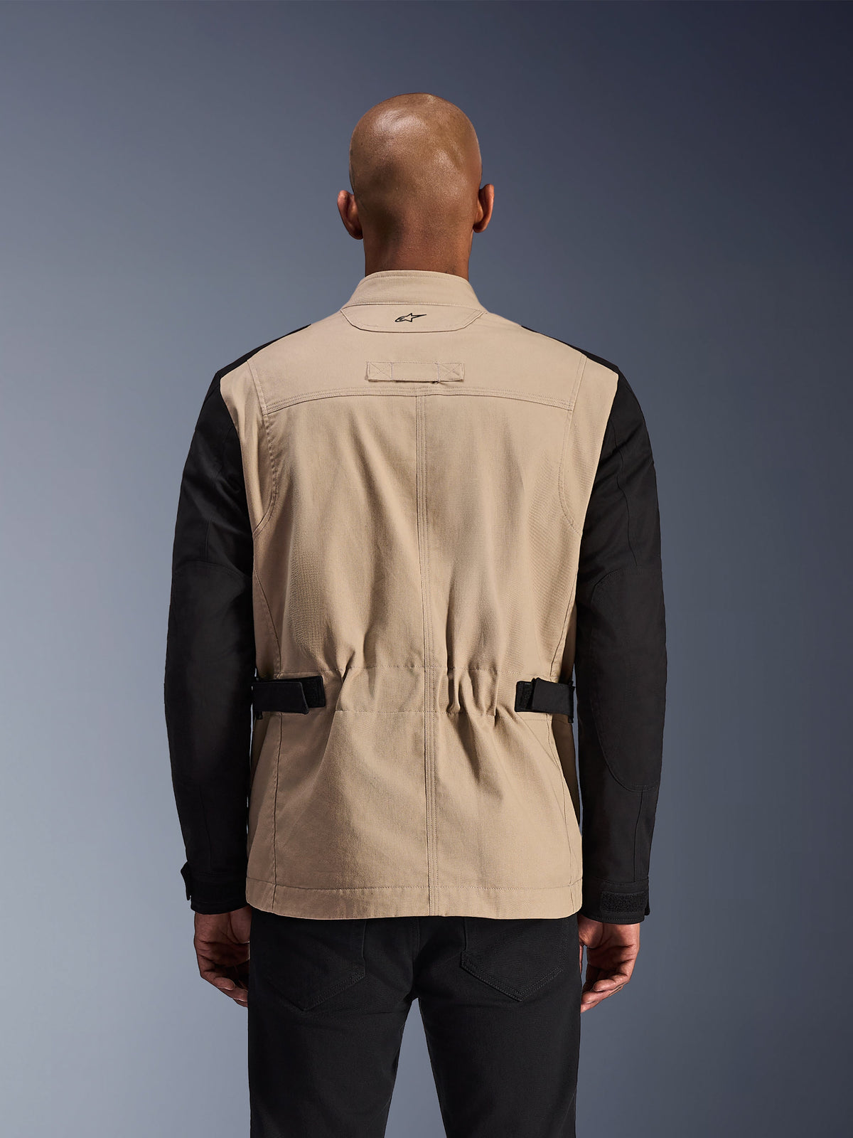 Alpinestars Dice Jacket, stedelijke motorjas, aluminum en zwart, achteraanzicht op een model, voorzien van geplooide schouders voor bewegingsvrijheid, verstelbare tailleriemen en een robuuste constructie van polykatoen twill.