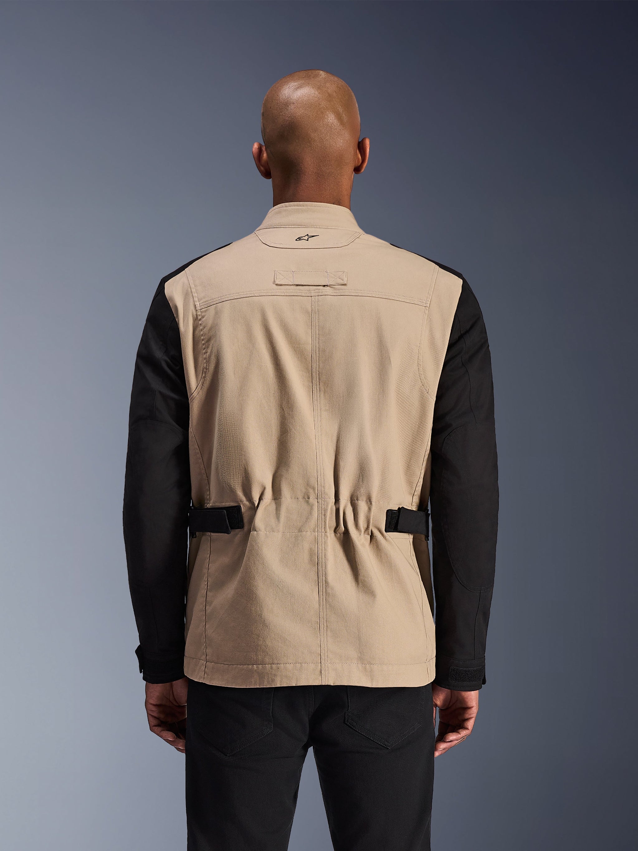 Alpinestars Dice Jacket, stedelijke motorjas, aluminum en zwart, achteraanzicht op een model, voorzien van geplooide schouders voor bewegingsvrijheid, verstelbare tailleriemen en een robuuste constructie van polykatoen twill.