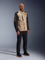 Alpinestars Dice Jas, stedelijke motorjas, Aluminum Black en Tan, tweekleurig ontwerp met zwarte mouwen en een khaki torso, gedragen door een model met zwarte broek en zwarte sneakers, op werkkleding geïnspireerde esthetiek met functionele zakken en geborduurd logo op de mouw.