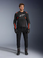 Mannelijk model draagt Alpinestars T-SPS Air v2 jas, zwarte textiele motorjas met Red Fluo accenten, wit logo op de borst, gedragen met zwarte broek, handschoenen en laarzen, urban sport rijstijl