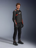 Mannelijk model in Alpinestars T-Sps Air v2 Jas, zwart met Red Fluo accenten, gecombineerd met een zwarte motorbroek, zwarte handschoenen en laarzen, sportief ontwerp met mesh-panelen en witte Alpinestars-logo's