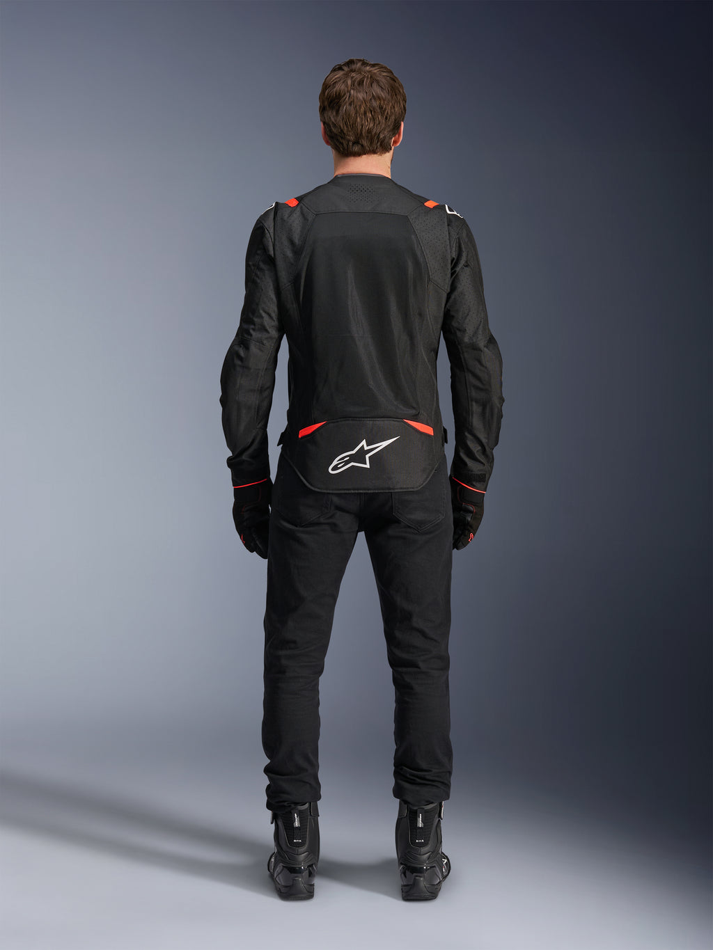 Alpinestars T-SPS Air v2 Jas in zwart en rood fluo, achteraanzicht met grote mesh ventilatiepanelen en wit Alpinestars-logo op de onderrug, gedragen met zwarte motorbroek en laarzen