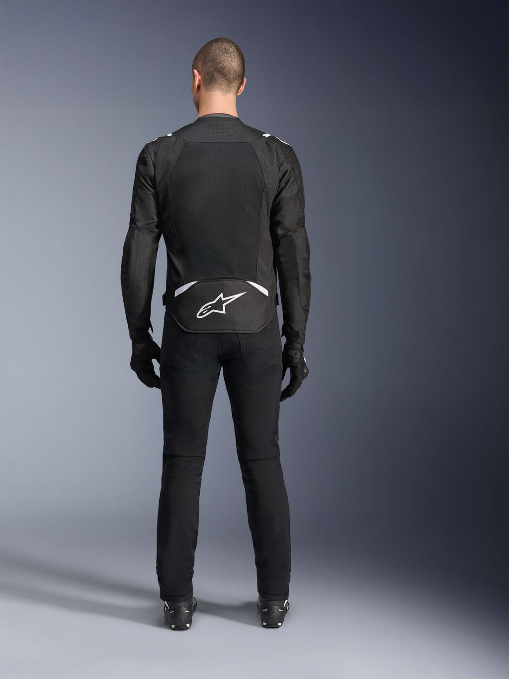 Alpinestars T-Sps Air V2 Jas, achteraanzicht, zwart-witte textiele motorjas, voorzien van een groot mesh rugpaneel voor maximale luchtstroom en wit Astars-logo op de onderrug, gedragen met een zwarte motorbroek en handschoenen