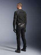 Alpinestars T-Sps Air V2 Jas, textiele motorjas, zwart, achteraanzicht met groot mesh ventilatiepaneel en wit Alpinestars-logo op de onderrug, gecombineerd met een zwarte motorbroek en handschoenen voor een sportieve urban look.