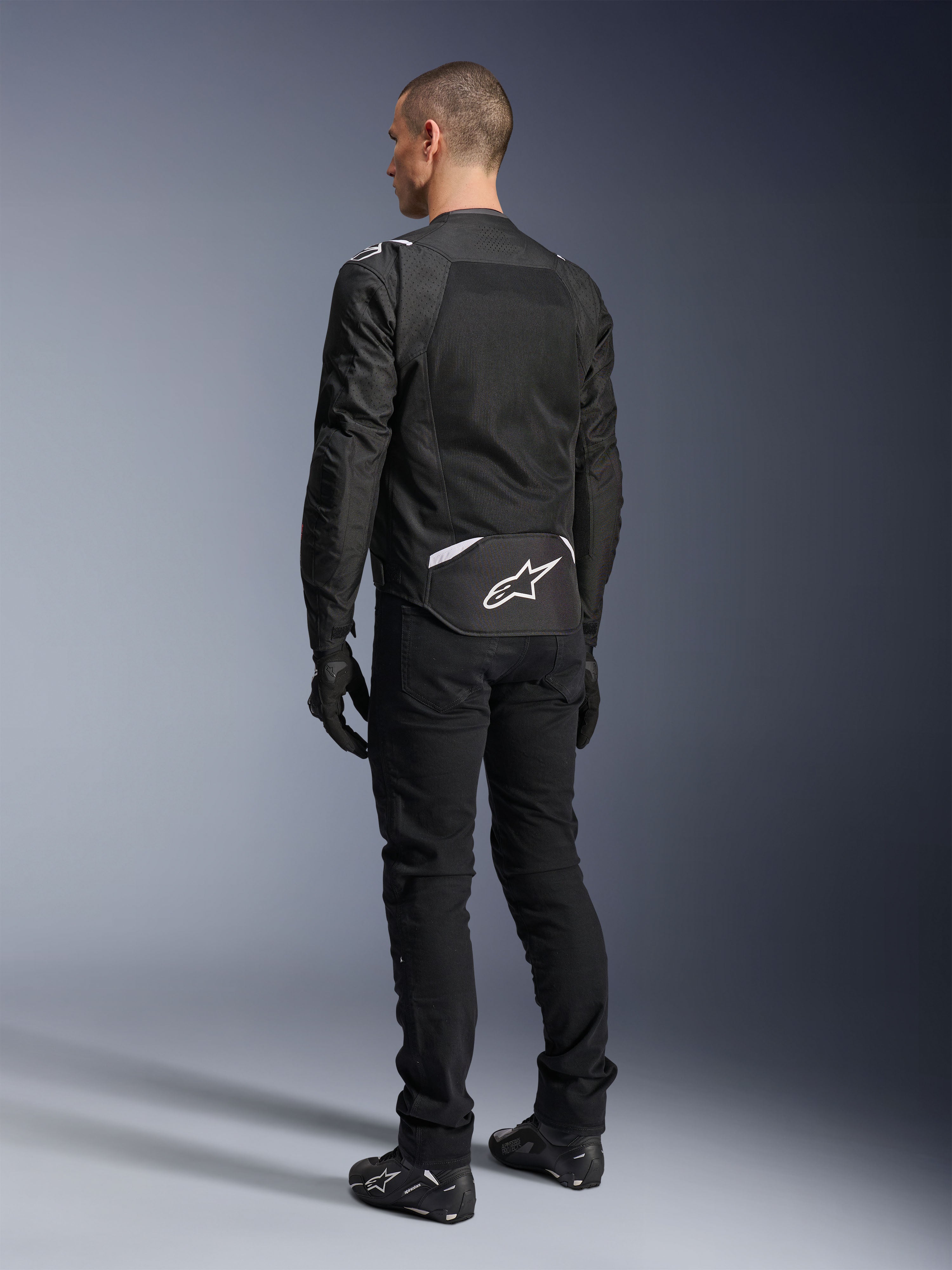 Alpinestars T-Sps Air V2 Jas, textiele motorjas, zwart, achteraanzicht met groot mesh ventilatiepaneel en wit Alpinestars-logo op de onderrug, gecombineerd met een zwarte motorbroek en handschoenen voor een sportieve urban look.