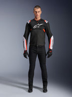 Mannelijk model draagt Alpinestars T-Sps Air V2 Jas in Black White Red Fluo, voorzien van grote tech mesh-panelen en opvallende witte logo's op de borst en mouwen, gecombineerd met een zwarte technische motorbroek en handschoenen, urban sport motorkleding