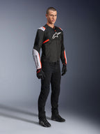 Alpinestars T-Sps Air V2 Jas, Black White Red Fluo, gedragen door een mannelijk model met zwarte motorbroek en handschoenen, textiele motorjas met grote mesh-panelen, witte schouder- en onderarmgedeelten en een opvallend Alpinestars logo op de borst.