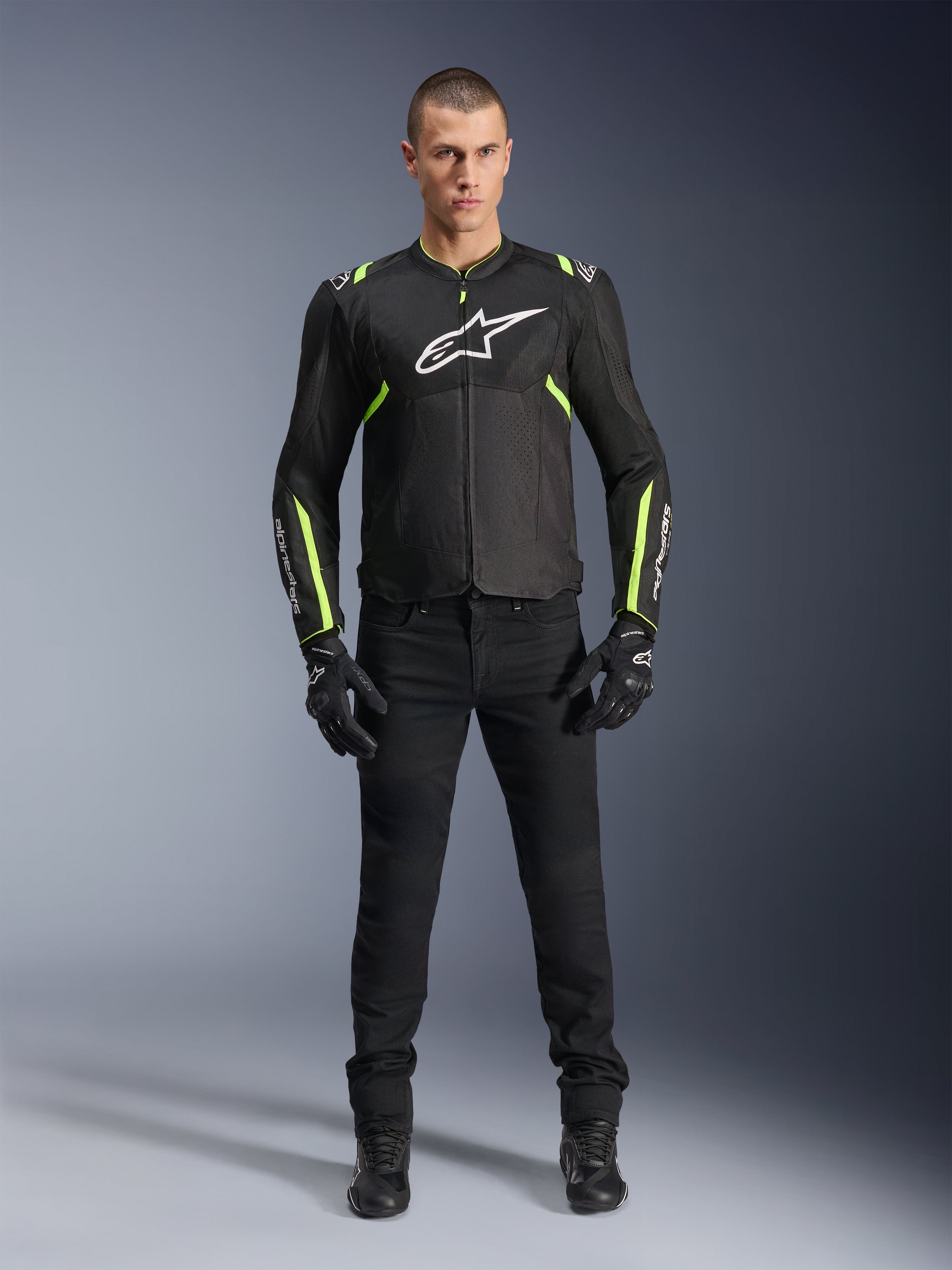 Alpinestars T-Sps Air V2 Jas, Zwart en Geel Fluo, textiele motorjas met mesh-panelen, gedragen door mannelijk model met zwarte broek en handschoenen, voorzien van wit Alpinestars-logo op de borst, urban sport motorkleding