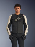Alpinestars T-SPS Air V2 motorjas, zwart en mastic aluminium, mannelijk model draagt jas met zwarte broek en handschoenen, mesh-panelen voor ventilatie, groot Alpinestars-logo op de borst, sportieve nauwsluitende pasvorm