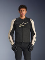 Alpinestars T-SPS Air V2 motorjas, zwart en mastic aluminium, mannelijk model draagt jas met zwarte broek en handschoenen, mesh-panelen voor ventilatie, groot Alpinestars-logo op de borst, sportieve nauwsluitende pasvorm