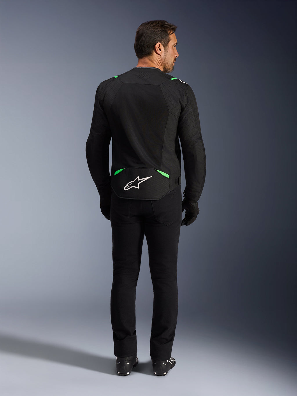 Alpinestars T-SPS Air V2 Jas, motorjas, zwart en fluo groen, achteraanzicht met wit logo op de onderrug, gedragen met bijpassende zwarte broek en laarzen, geventileerd mesh-ontwerp voor sportief rijden